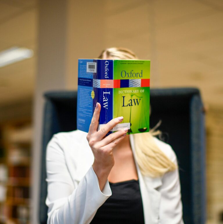 Blonde woman reading the Oxford Dictionary of Law in a university library setting.